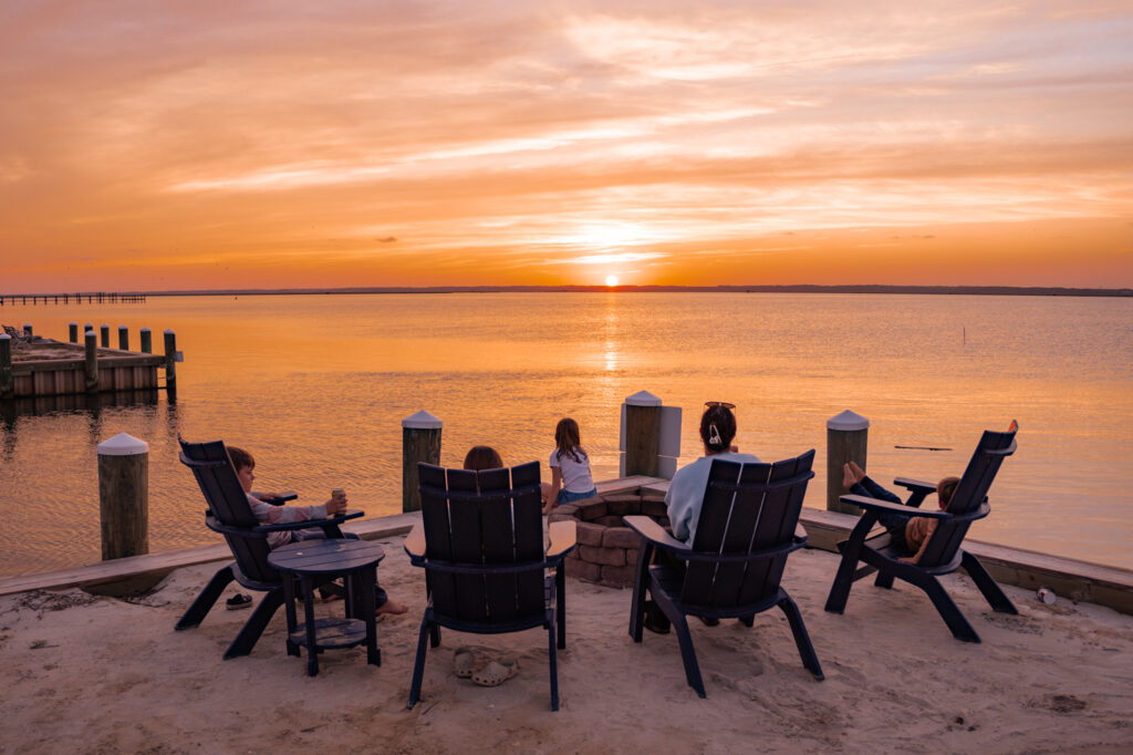 family sitting at firepit watching sunset